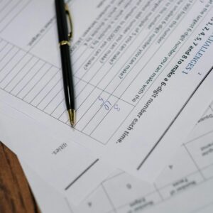 Black pen resting on printed business forms and worksheets