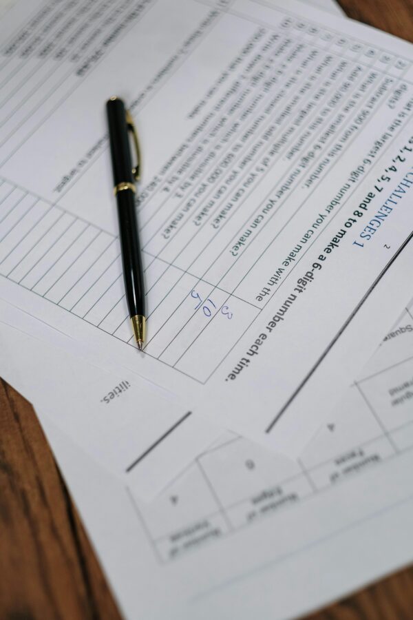 Black pen resting on printed business forms and worksheets